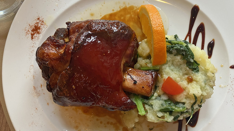 glazed pork knuckle plated with orange slice and vegetable mash