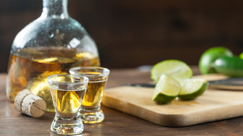 Tequila in shot glasses near a bottle and lime wedges on a cutting board