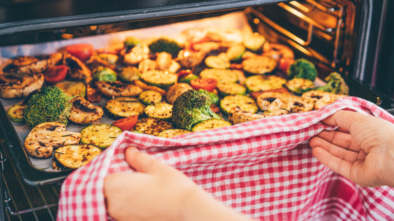 Assorted vegetables on.a sheet pan being placed in an oven