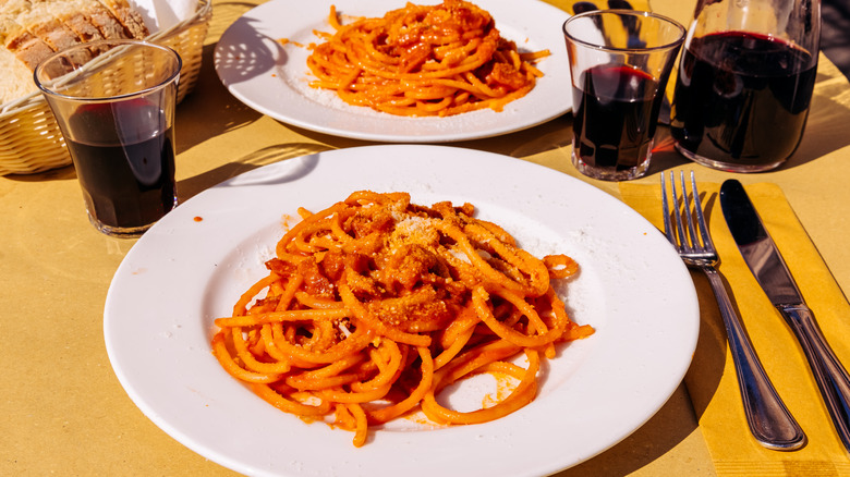 Two plates of pasta amatriciana and glasses of red wine