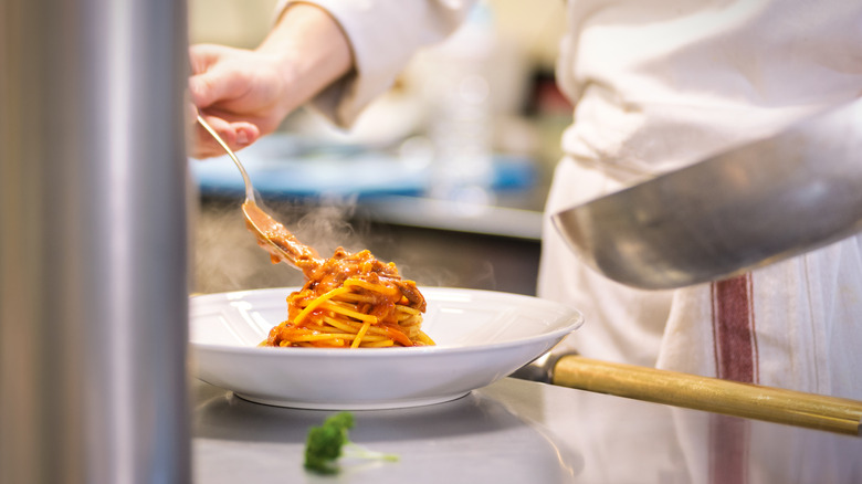 A chef plating spaghetti with red sauce on white plate