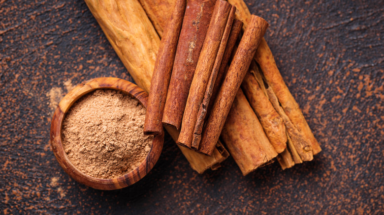 cinnamon sticks next to small wooden bowl of ground cinnamon