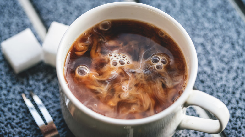 A white cup of coffee with creamer mixing into it