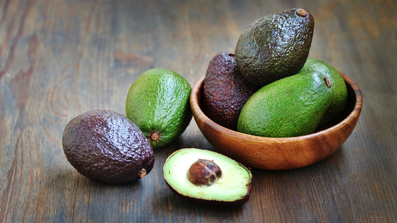 Different varieties of avocados, some in a wooden bowl and some on the table