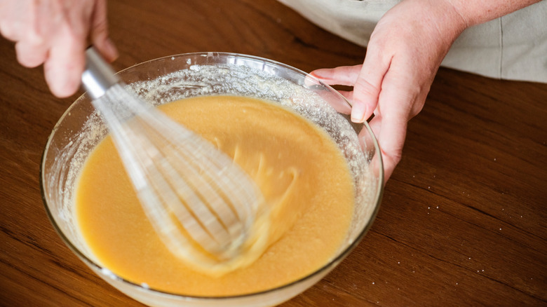 Close-up of hands mixing batter in a glass bowl