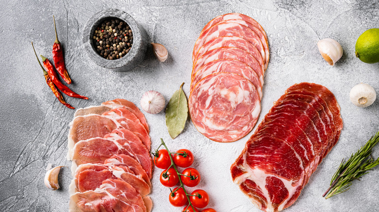 Pancetta and prosciutto on a grey surface with seasonings