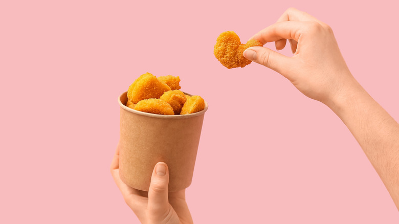 Hands picking chicken nugget out of small paper bucket