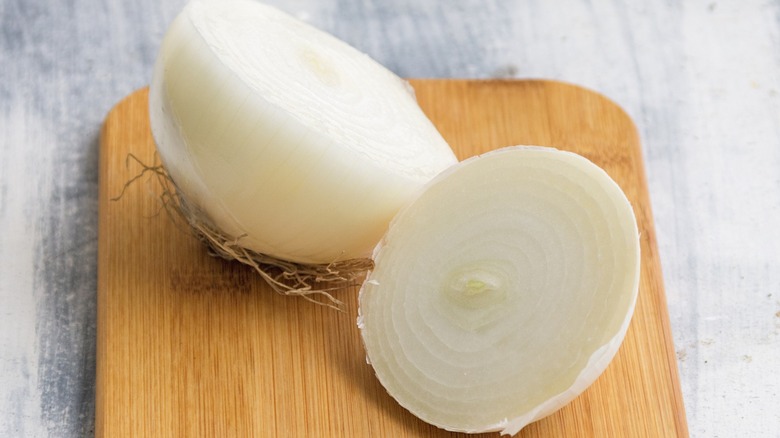 A white onion cut in half on a wooden board.