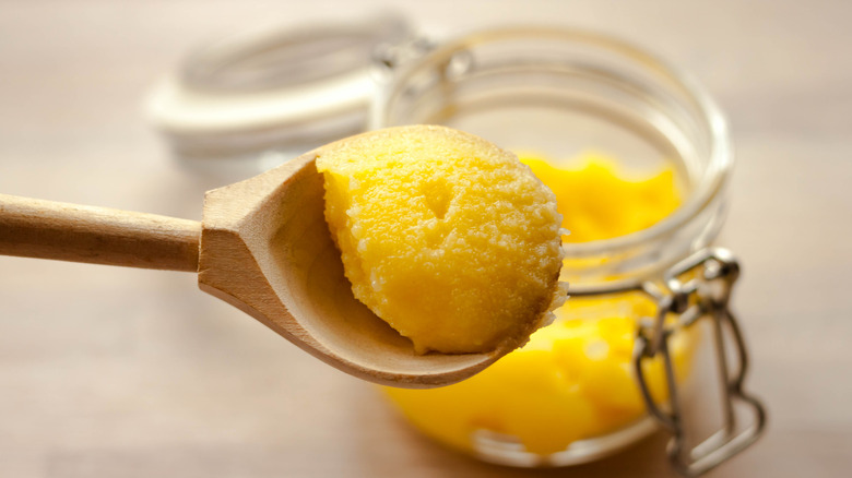 Desi ghee  in glass jar with wooden spoonful on natural light beige background