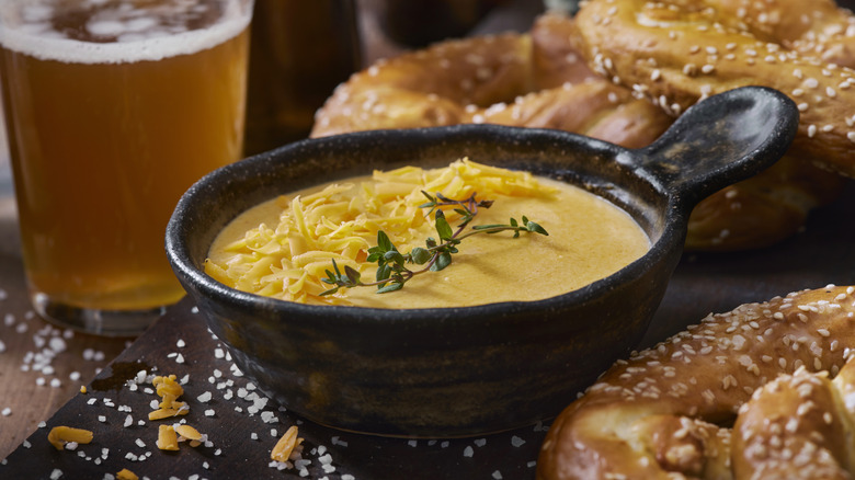 warm beer cheese in a crock with a pint of beer and pretzels