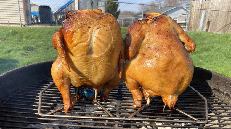 two whole chickens on beer cans on a grill