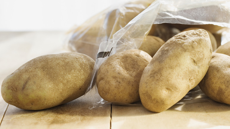 Potatoes spill out of a plastic bag onto a wooden table