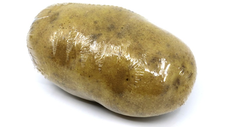 Single potato wrapped in plastic on white background