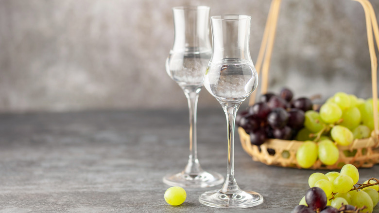 A pair of tulip glasses full of grappa, with a basket of grapes.