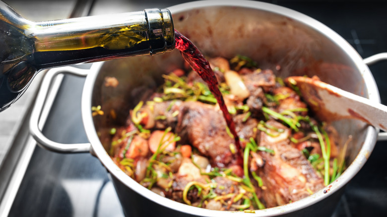 Red wine being poured into a large pot with food in it