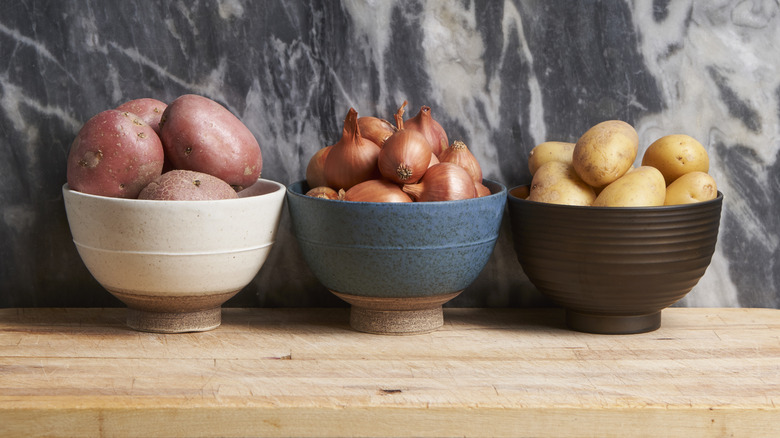 Potatoes and onions sitting in separate bowls.