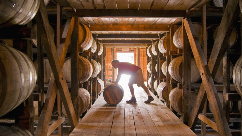 A man rolling a whiskey barrel at a distillery.