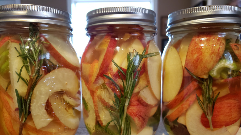 Three mason jars with pickled apples, rosemary, and anise.