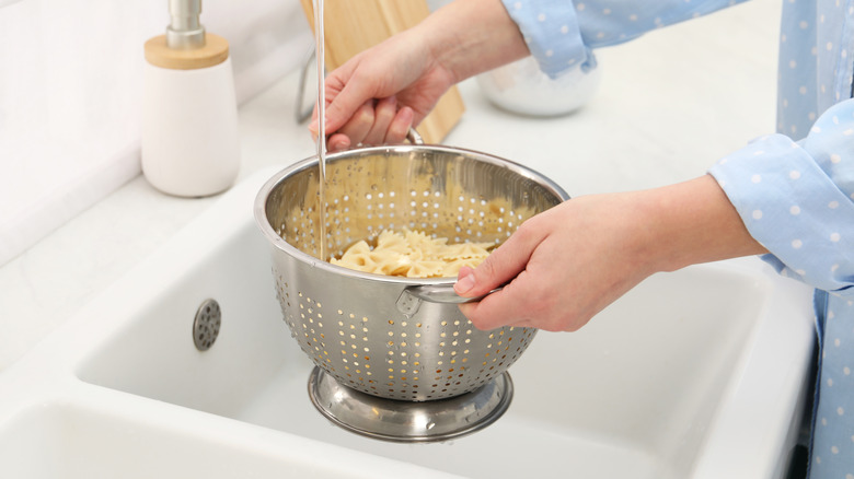 A woman rinsing a colander of pasta in the sink