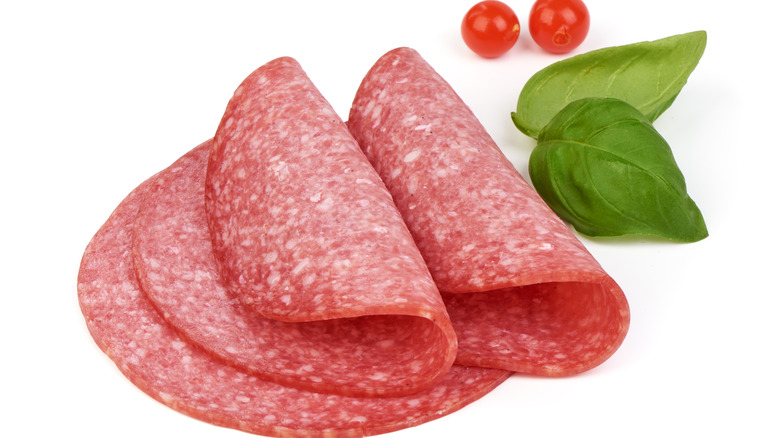 Three slices of salami with basil leaves and cherry tomatoes on white background