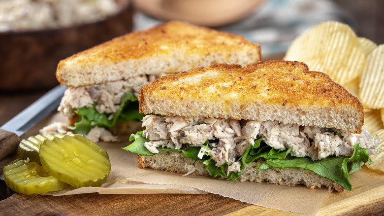 Tuna salad sandwich on toasted bread with pickles and chips