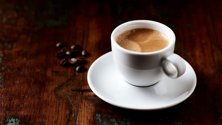 A white coffee mug sitting on a white saucer with coffee beans surrounding it