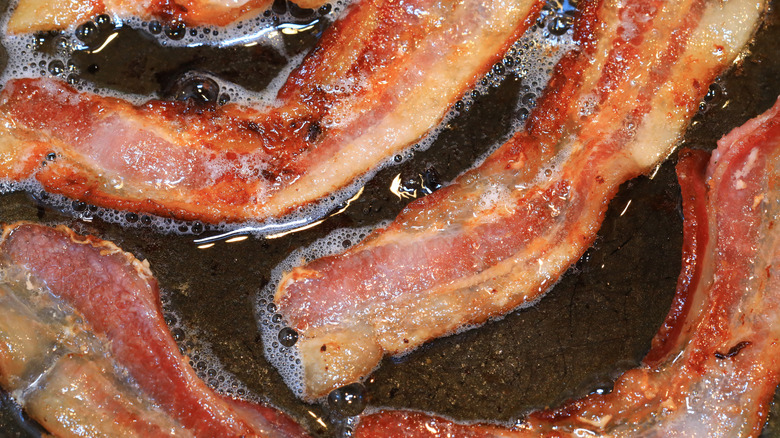 Four slices of streaky bacon cook in grease on a heated surface