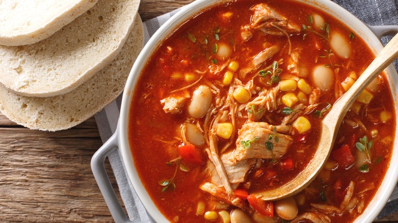 A small pot of Brunswick stew with wooden spoon in it and bread on the side