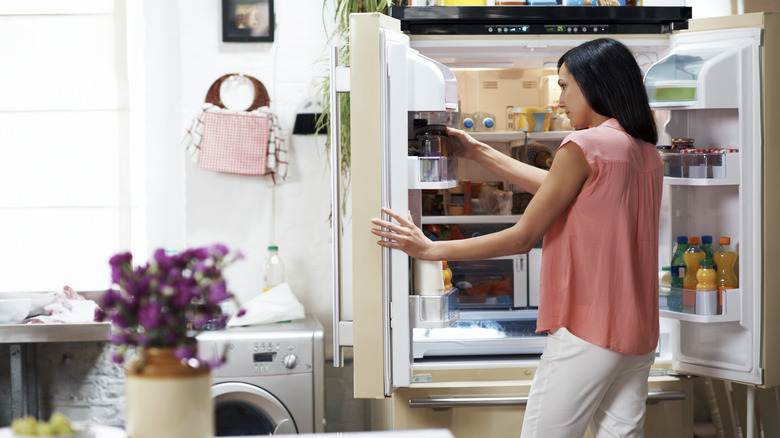 Woman in front of an open fridge putting something away