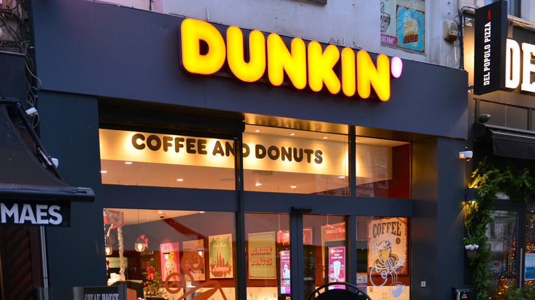 A Dunkin' location with the letters lit in orange and the apostrophe lit in pink, and a lit interior that also says "coffee and donuts"