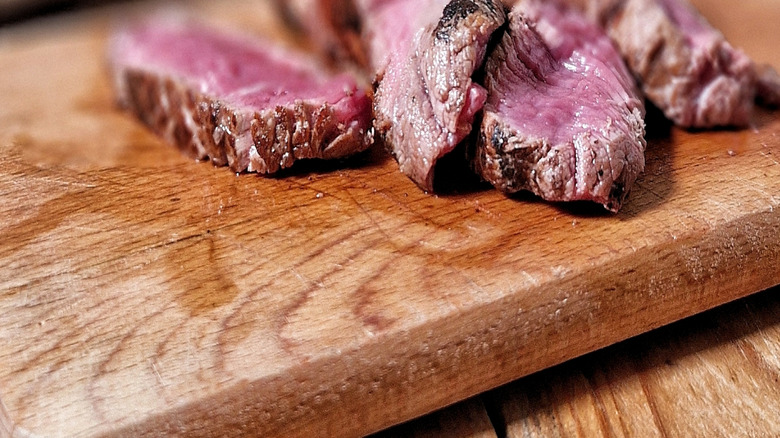 Sliced beef flank steak cooked medium rare on a wooden cutting board