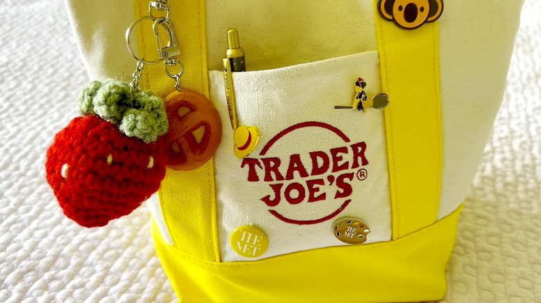 Close up of a yellow and cream Trader Joe's tote bag with keychains and pins