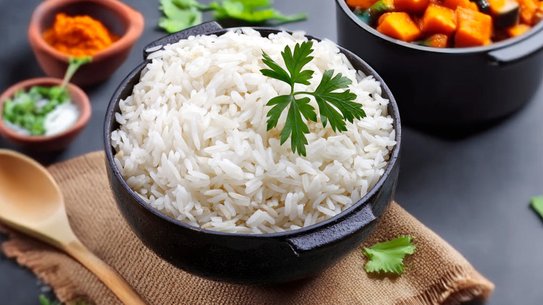 A black dish of cooked white rice topped with a herb sprig