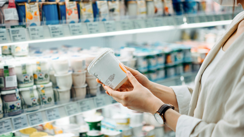 A person in a grocery store looking at the label on a container of yogurt