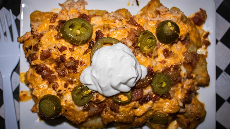 A plate of tater tots with cheese, sour cream, and jalapeños