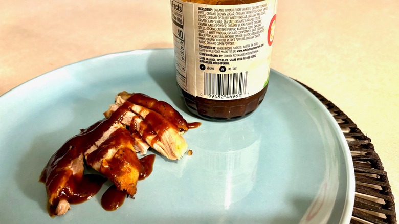 Some chicken with barbecue sauce on a plate by a sauce bottle