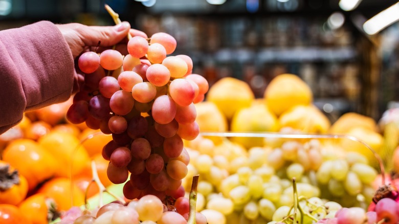 A hand holding a bunch of grapes at a grocery store