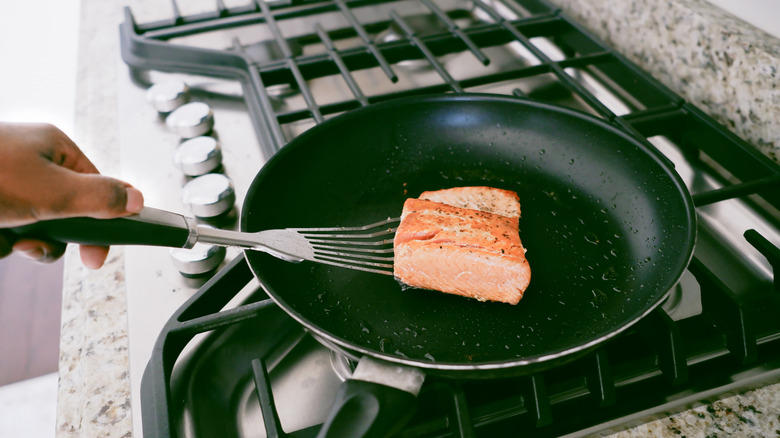 Person cooking salmon with a fish spatula