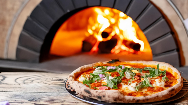 A pizza being pulled out of a wood burning oven.