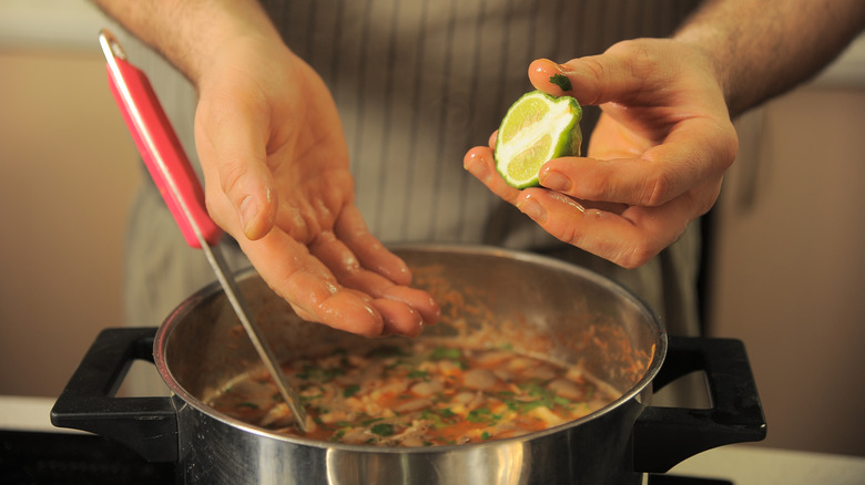 Person's hands squeezing lime juice into a pot of soup