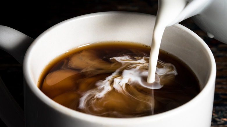 Milk is being poured into a cup of coffee.