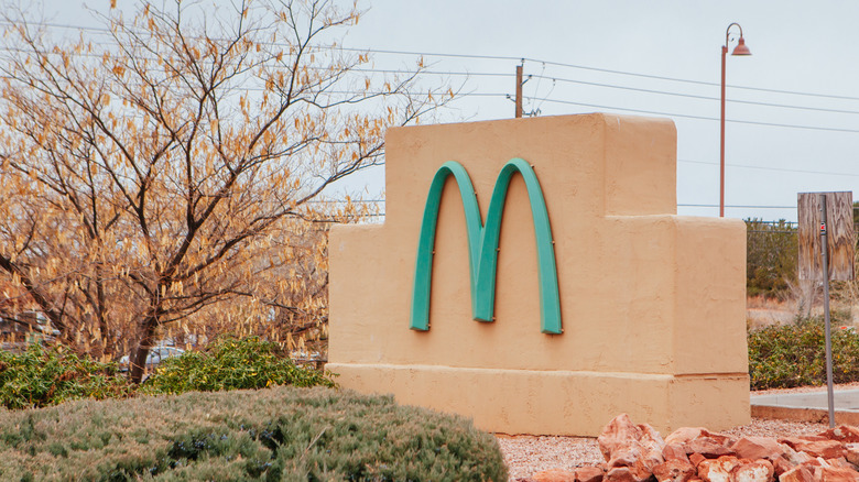 A turquoise 'M' sign for McDonald's on a dusty red structure