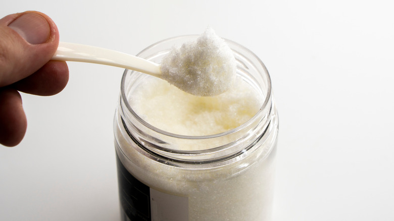 A hand holding a heaping spoonful of monosodium glutamate, also known as MSG, above a jar.