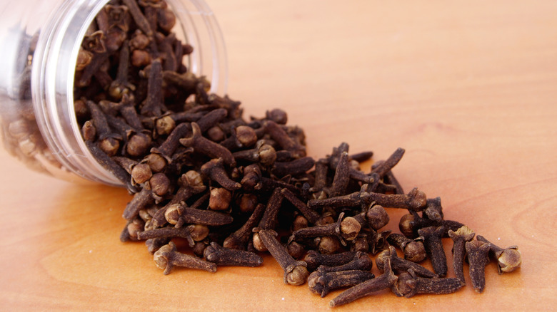 Whole cloves spilling from a tipped over glass jar