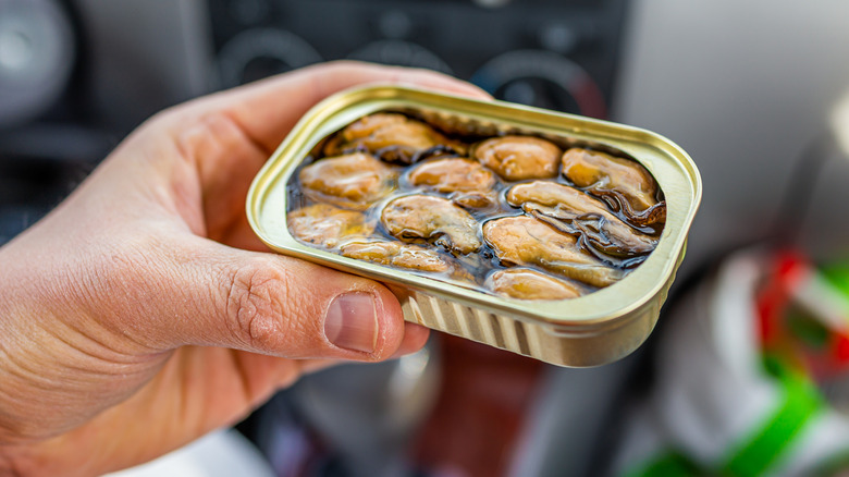 A hand holds an open can of oysters.