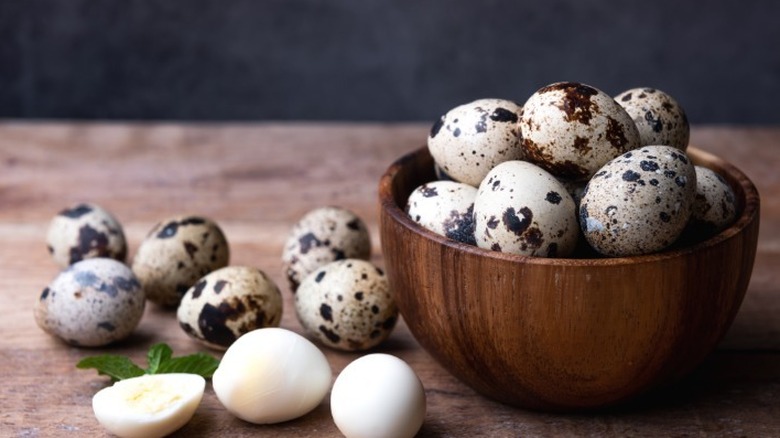 Quail eggs sitting in a bowl and lying on a counter.