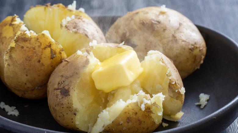 Baked potatoes cut open with steam coming out and butter melting