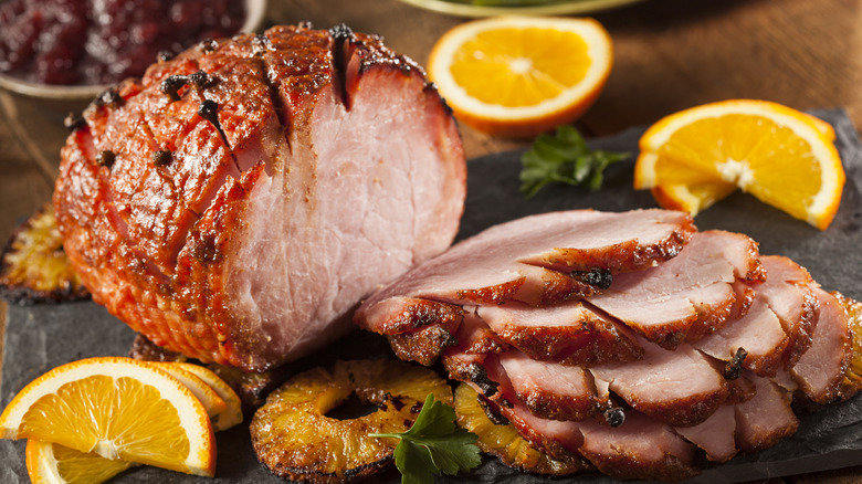 A roasted ham, sliced on a cutting board.