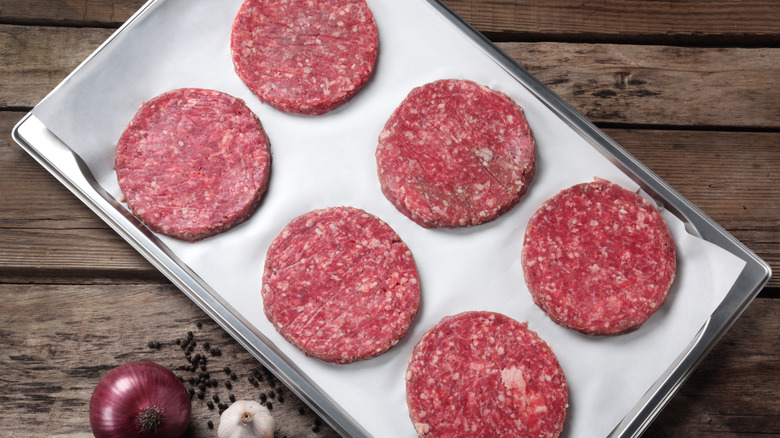 uncooked burger patties on a parchment-line baking sheet set on a rustic wood table