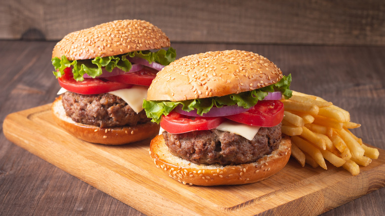 two cheeseburgers and a pile of fries on top of a wooden cutting board